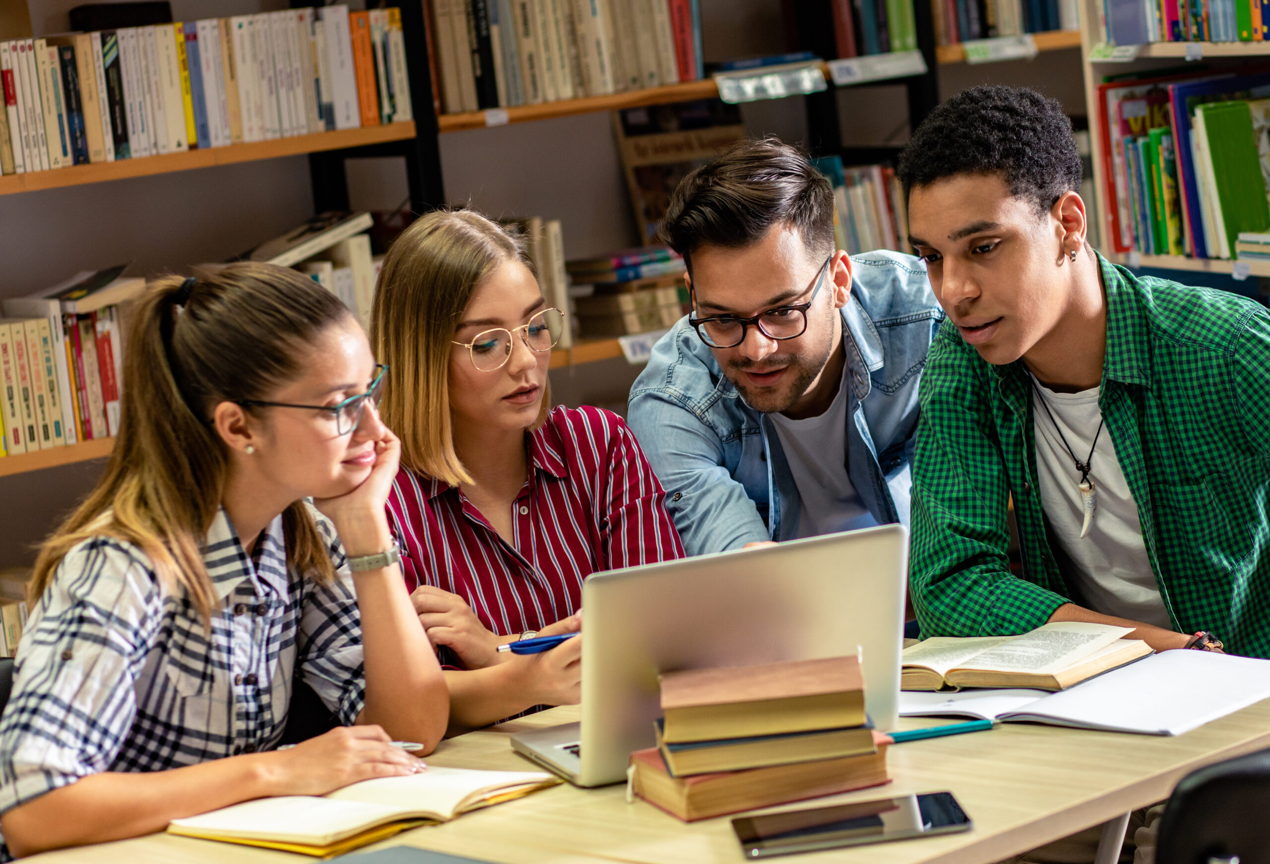 Four young students study in the school library, they using lapt