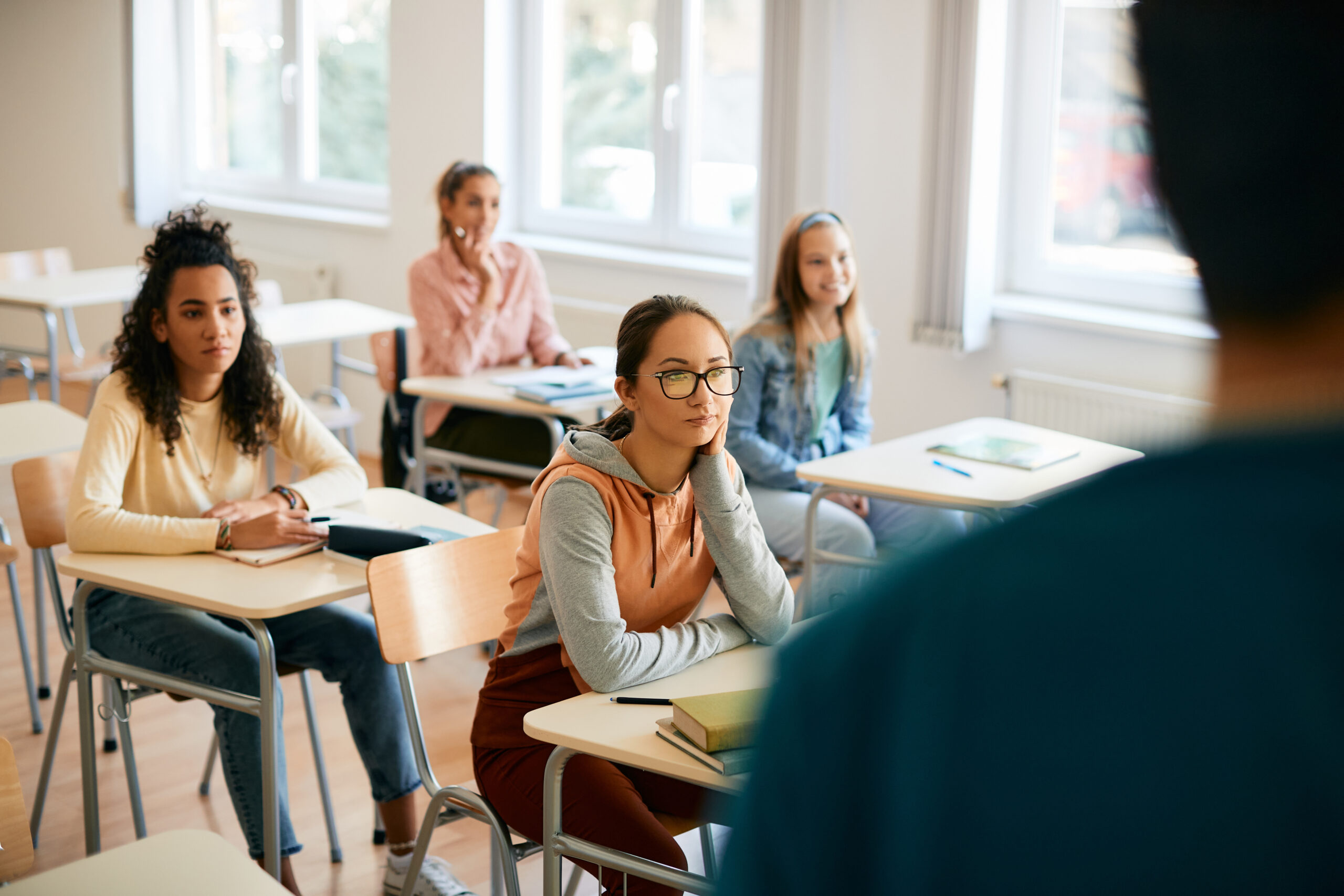 Teenage girl and her classmates paying attention during teacher's lecture on class in high school.